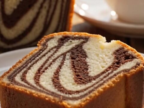 A thick, plush slice of marble loaf cake with a visible black-and-white zebra swirl being cut on a marble surface.