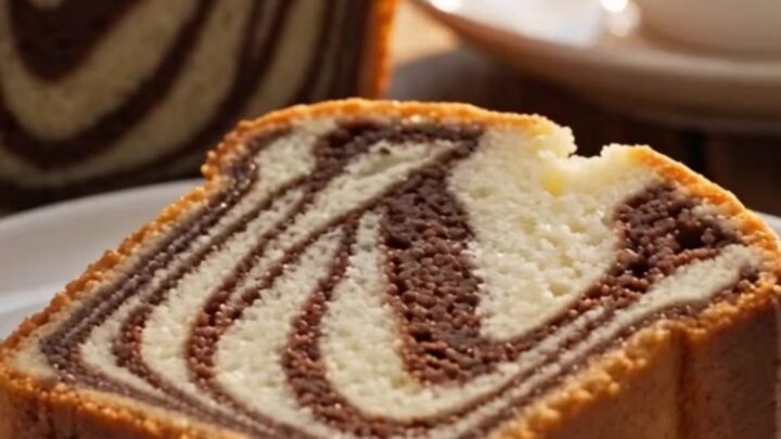 A thick, plush slice of marble loaf cake with a visible black-and-white zebra swirl being cut on a marble surface.