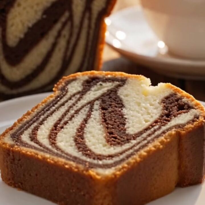 A thick, plush slice of marble loaf cake with a visible black-and-white zebra swirl being cut on a marble surface.