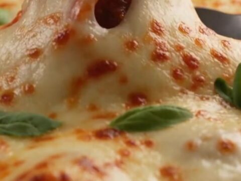 A close-up shot of a large metal spoon scooping out cheesy, meatball-stuffed jumbo pasta shells from a skillet.