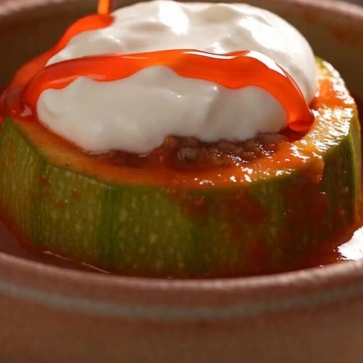 A close-up view of a tender, glazed round zucchini bowl sitting in a bubbling, rich red tomato sauce.