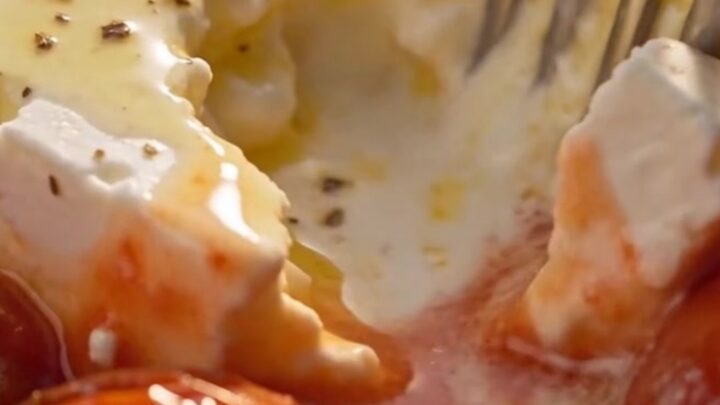 A serving spoon lifts a steaming portion of tender shell pasta covered in a rich pink tomato-cream sauce with melted feta.