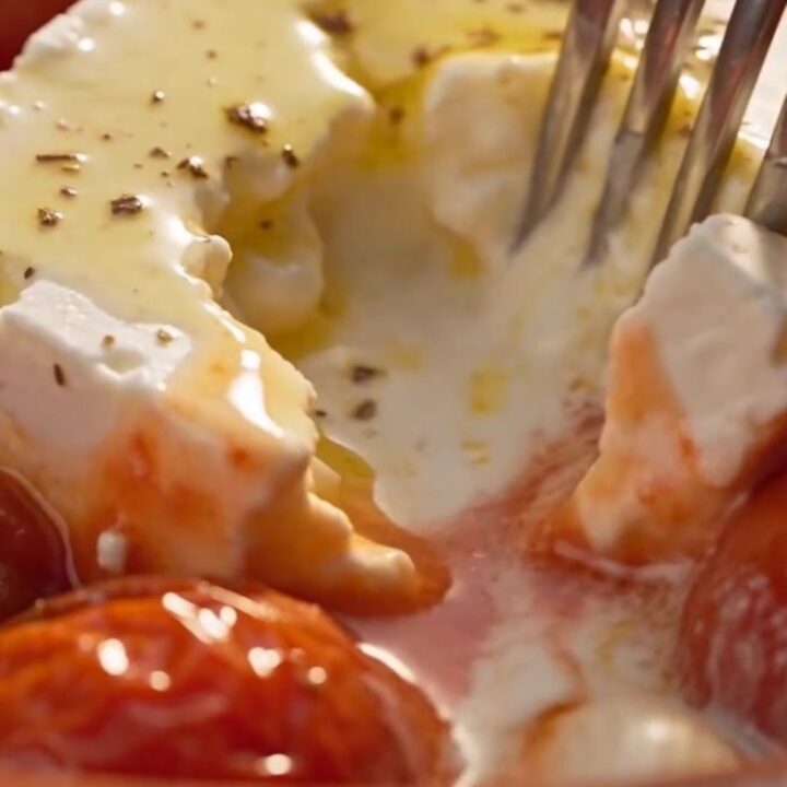 A serving spoon lifts a steaming portion of tender shell pasta covered in a rich pink tomato-cream sauce with melted feta.