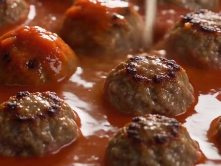 A close-up of a skillet filled with baked rigatoni, meatballs, and melted, stretchy mozzarella cheese.