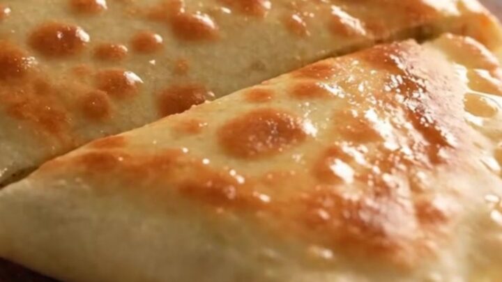 A close-up of a golden-brown Turkish gözleme being torn open, revealing a steaming potato and cheese filling.