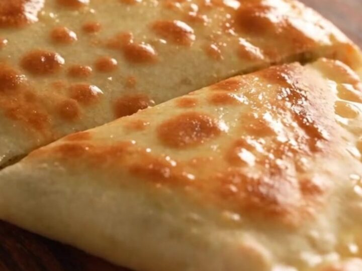 A close-up of a golden-brown Turkish gözleme being torn open, revealing a steaming potato and cheese filling.