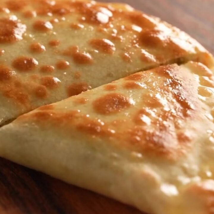 A close-up of a golden-brown Turkish gözleme being torn open, revealing a steaming potato and cheese filling.
