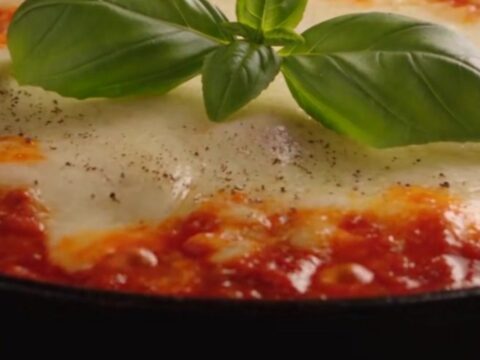 A close-up of a spatula lifting a single lasagna roll-up from a skillet, showing long cheese pulls.