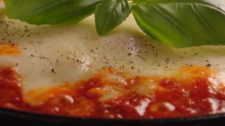 A close-up of a spatula lifting a single lasagna roll-up from a skillet, showing long cheese pulls.