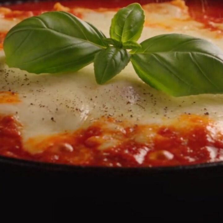 A close-up of a spatula lifting a single lasagna roll-up from a skillet, showing long cheese pulls.