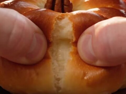 A close-up shot of a golden-brown pumpkin-shaped brioche bun being pulled apart to reveal a stretchy cheese filling.
