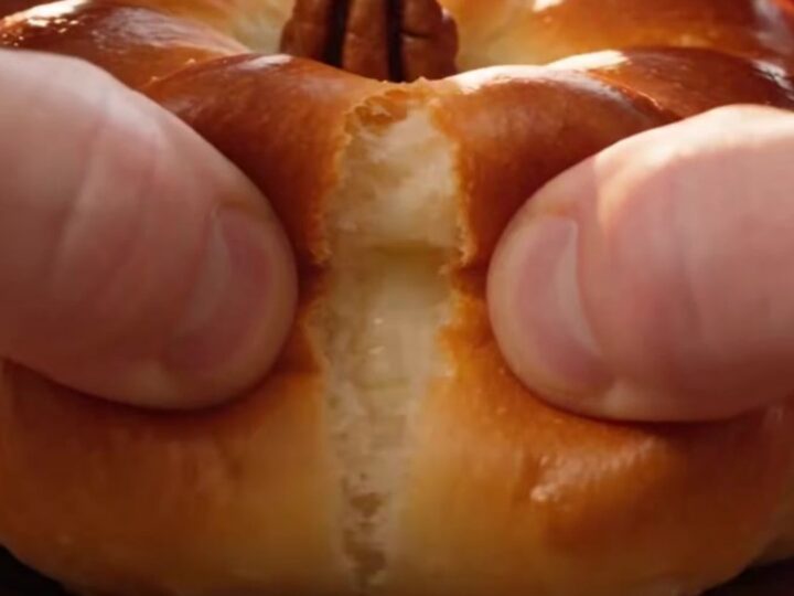 A close-up shot of a golden-brown pumpkin-shaped brioche bun being pulled apart to reveal a stretchy cheese filling.