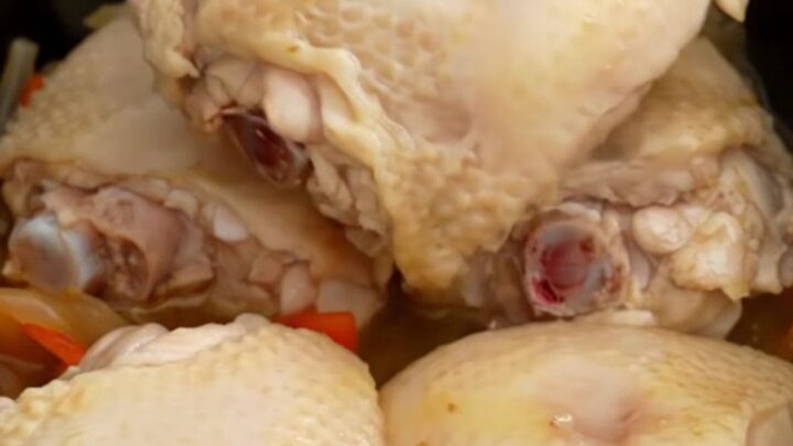 A top-down view of a slow cooker filled with chicken thighs, colorful bell peppers, and red onions ready to be cooked.