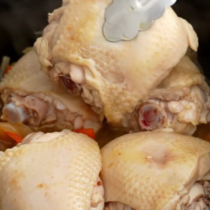 A top-down view of a slow cooker filled with chicken thighs, colorful bell peppers, and red onions ready to be cooked.