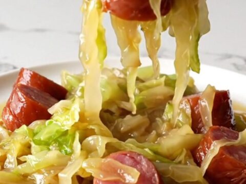 A close-up of tender green cabbage wedges and savory kielbasa coins served in a pool of golden brown butter broth.