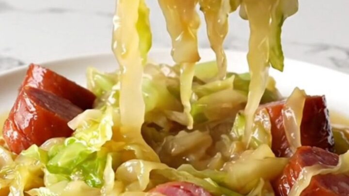 A close-up of tender green cabbage wedges and savory kielbasa coins served in a pool of golden brown butter broth.