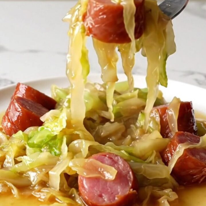 A close-up of tender green cabbage wedges and savory kielbasa coins served in a pool of golden brown butter broth.