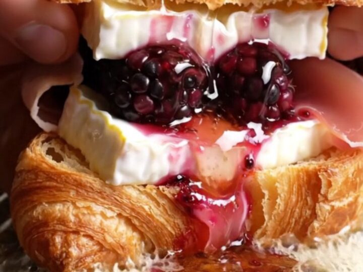 A close-up shot of a crispy golden croissant melt oozing with melted Brie and fresh blackberries.