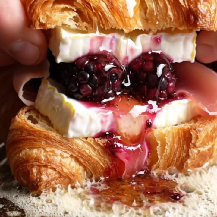A close-up shot of a crispy golden croissant melt oozing with melted Brie and fresh blackberries.
