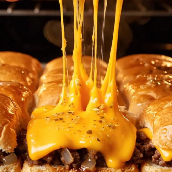 A close-up of a pull-apart garlic butter beef slider with melted cheddar cheese stretching as it is lifted from a pan.