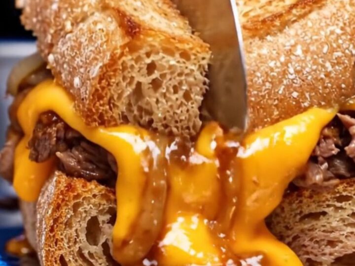 A close-up of a crispy Philly cheesesteak patty melt on sourdough bread with molten cheese dripping from the sides.