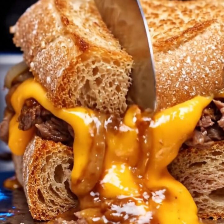 A close-up of a crispy Philly cheesesteak patty melt on sourdough bread with molten cheese dripping from the sides.