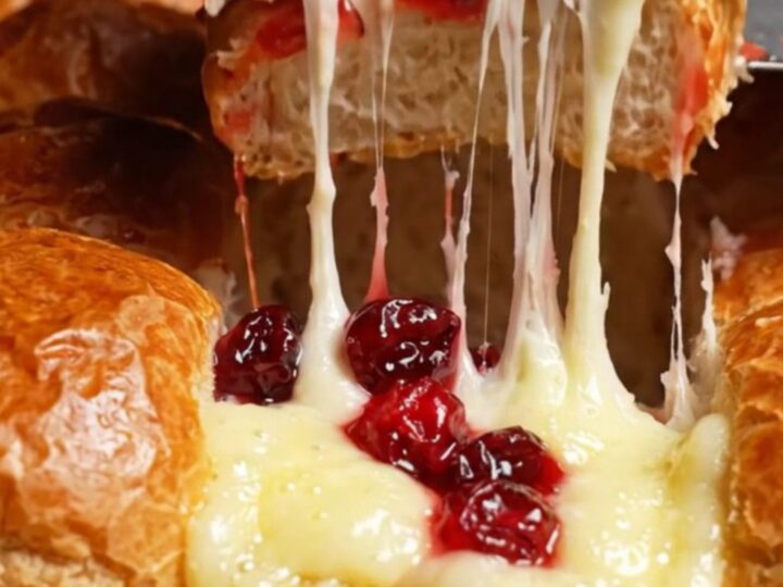 A close-up of warm, golden brown sliders with melted Brie and cranberry sauce spilling out.