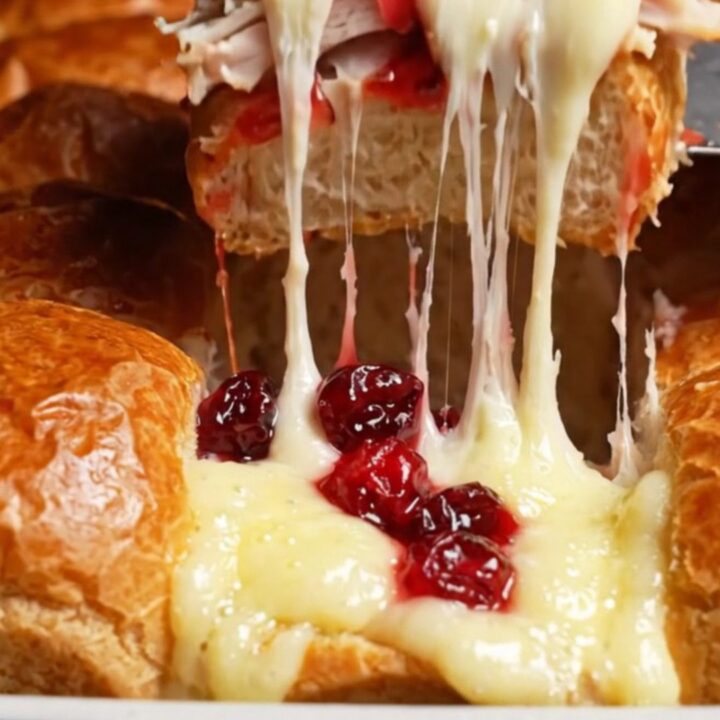A close-up of warm, golden brown sliders with melted Brie and cranberry sauce spilling out.