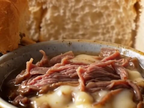 A stack of pull-apart French dip sliders with melted provolone and caramelized onions