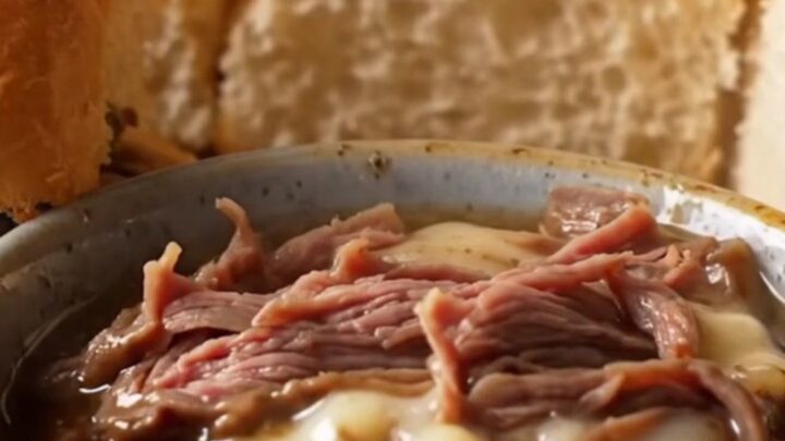 A stack of pull-apart French dip sliders with melted provolone and caramelized onions
