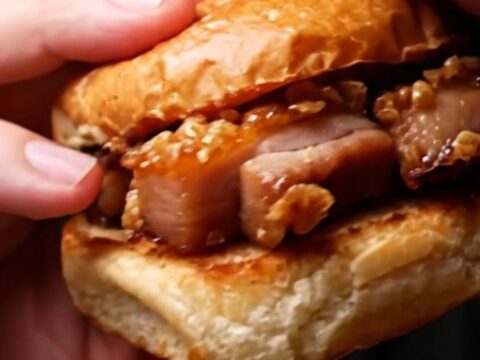 A close-up shot of a crispy pork belly slider with a glossy hoisin glaze on a toasted brioche bun.