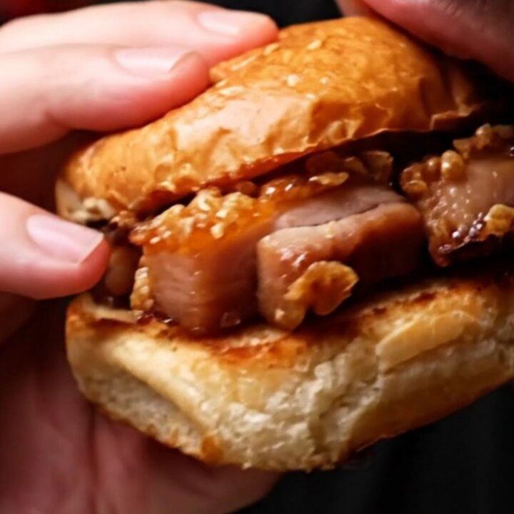 A close-up shot of a crispy pork belly slider with a glossy hoisin glaze on a toasted brioche bun.