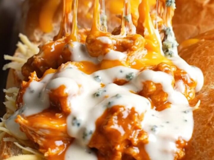 A close-up shot of a sheet pan filled with golden buffalo chicken sliders, with melted cheese pulling apart.