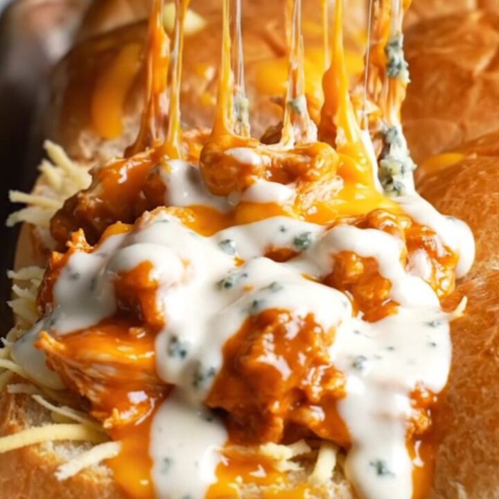 A close-up shot of a sheet pan filled with golden buffalo chicken sliders, with melted cheese pulling apart.