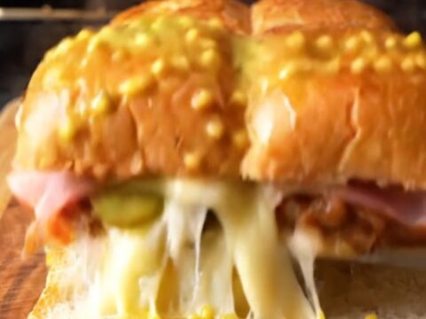 A close-up of a crispy, golden-brown Cuban slider with melted Swiss cheese oozing from the sides.
