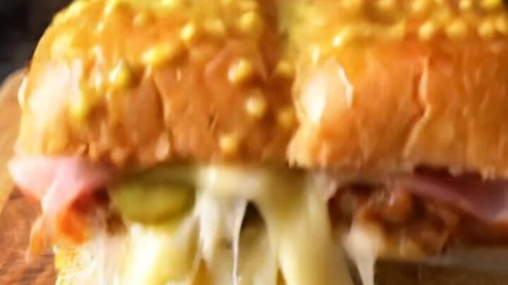 A close-up of a crispy, golden-brown Cuban slider with melted Swiss cheese oozing from the sides.