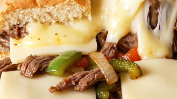 A macro shot of a pull-apart Philly cheesesteak slider showing juicy ribeye, melted cheese, and charred peppers.
