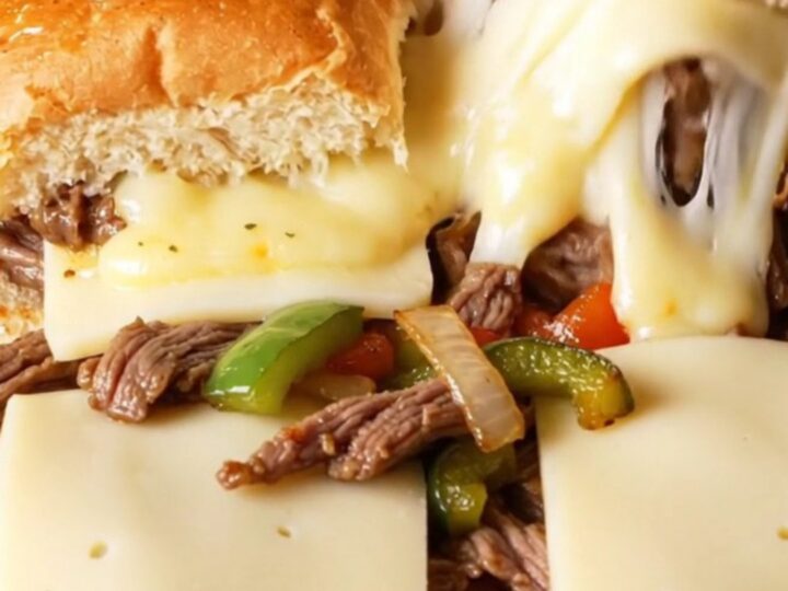 A macro shot of a pull-apart Philly cheesesteak slider showing juicy ribeye, melted cheese, and charred peppers.