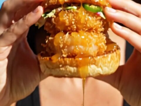 A close-up shot of a crispy coconut shrimp slider on a brioche bun with a vibrant mango habanero slaw.
