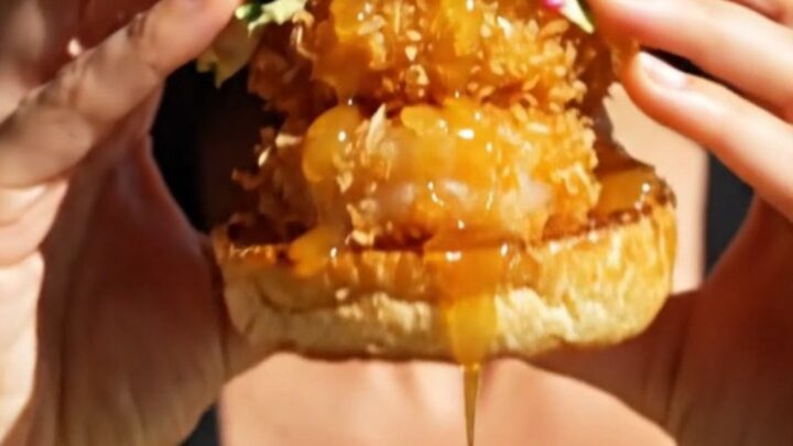 A close-up shot of a crispy coconut shrimp slider on a brioche bun with a vibrant mango habanero slaw.