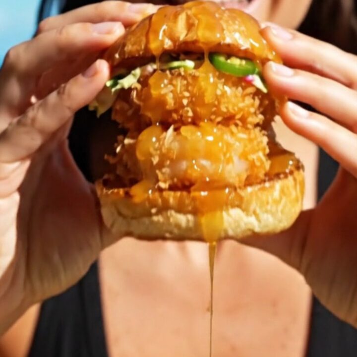 A close-up shot of a crispy coconut shrimp slider on a brioche bun with a vibrant mango habanero slaw.