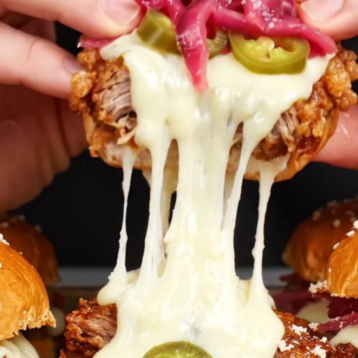 A close-up of crispy pork carnitas sliders on a rustic wooden board with a visible cheese pull.