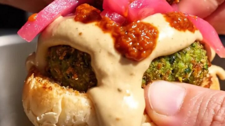 Close-up of a crispy green falafel slider on a toasted brioche bun with tahini sauce.