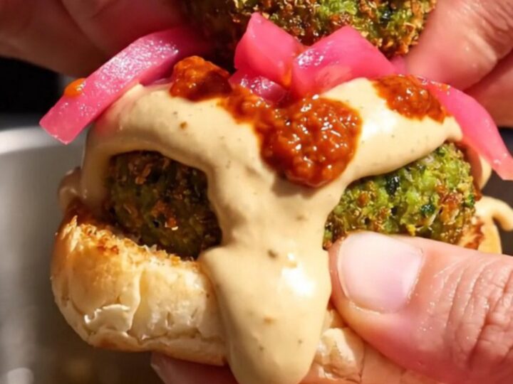 Close-up of a crispy green falafel slider on a toasted brioche bun with tahini sauce.