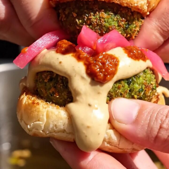 Close-up of a crispy green falafel slider on a toasted brioche bun with tahini sauce.