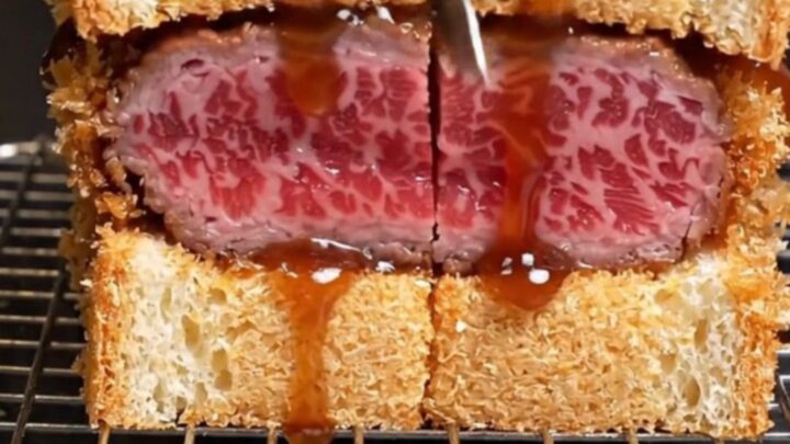A close-up of an A5 Wagyu katsu sando showing the ruby-rare meat and crispy golden panko crust.