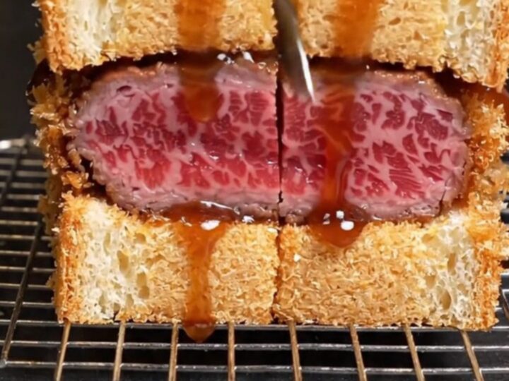 A close-up of an A5 Wagyu katsu sando showing the ruby-rare meat and crispy golden panko crust.