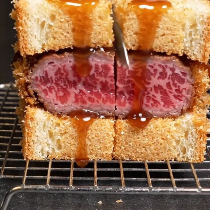 A close-up of an A5 Wagyu katsu sando showing the ruby-rare meat and crispy golden panko crust.