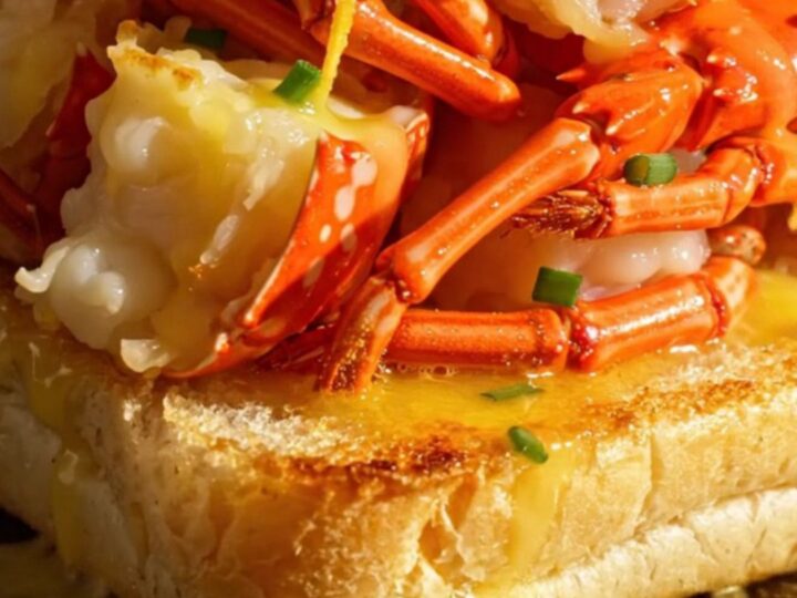 A close-up view of a golden-brown toasted split-top brioche roll overflowing with tender, butter-poached lobster meat.