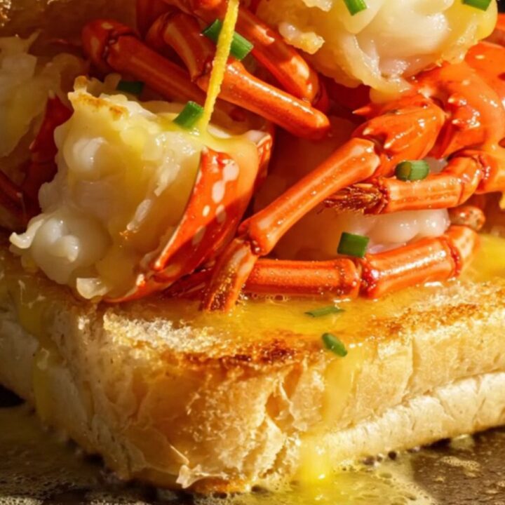 A close-up view of a golden-brown toasted split-top brioche roll overflowing with tender, butter-poached lobster meat.